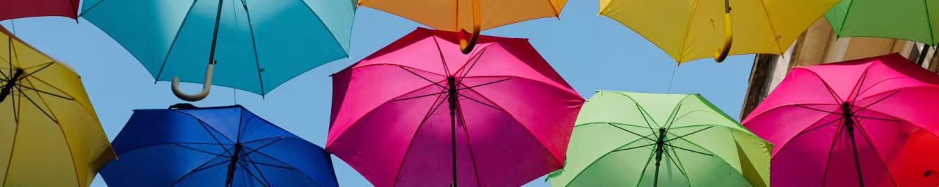Kleurrijke opengeslagen paraplu's zweven boven straat tegen blauwe lucht, symboliseert privacybeleid en geen geheimzinnigheid
